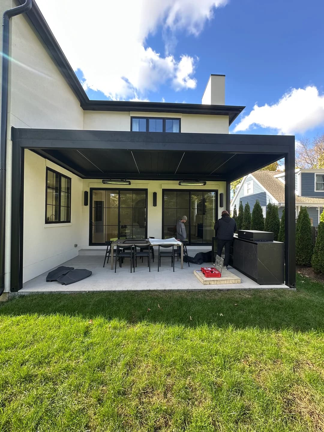Dark pergola frame adjoining a cream-colored home over a patio