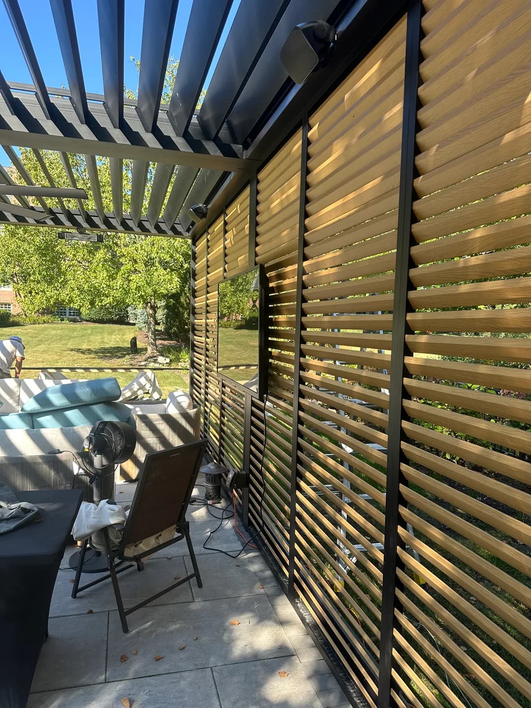 Dark pergola roof louvers beside wood privacy slats and patio seating